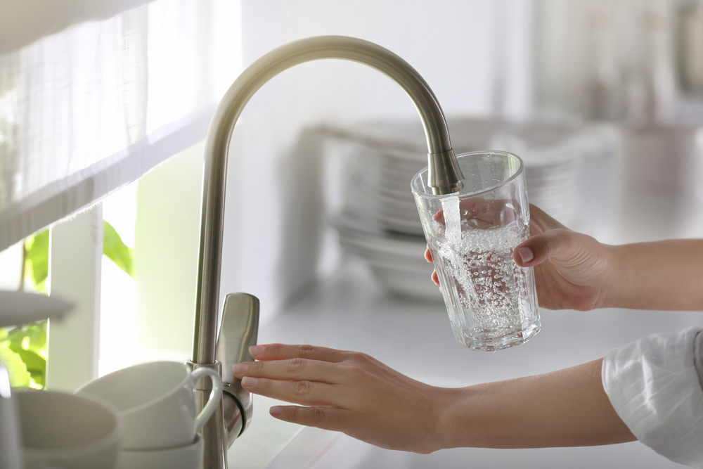 A closeup of someone pouring water into a glass from their kitchen faucet.