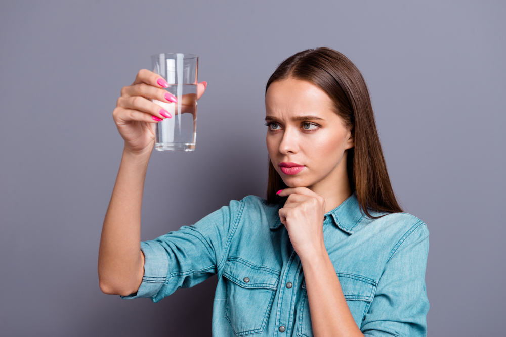 A woman holding a glass of water up and studying it.